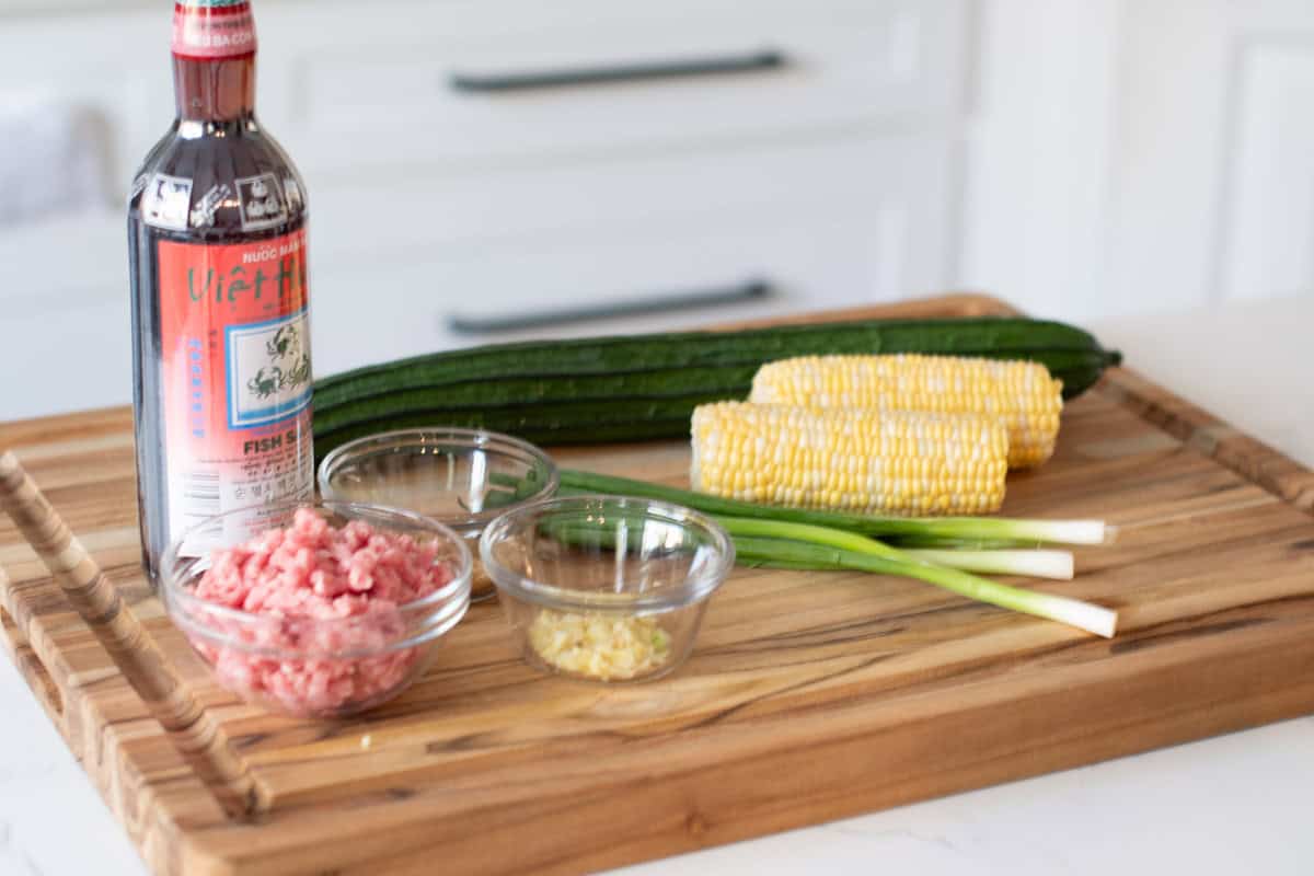 Ingredients Chinese Okra and Corn Stew on a cutting board including Chinese okra, Corn, Ground Pork, Diced Garlic, Chopped green onion, Brown Sugar, Ground black pepper, Fish sauce