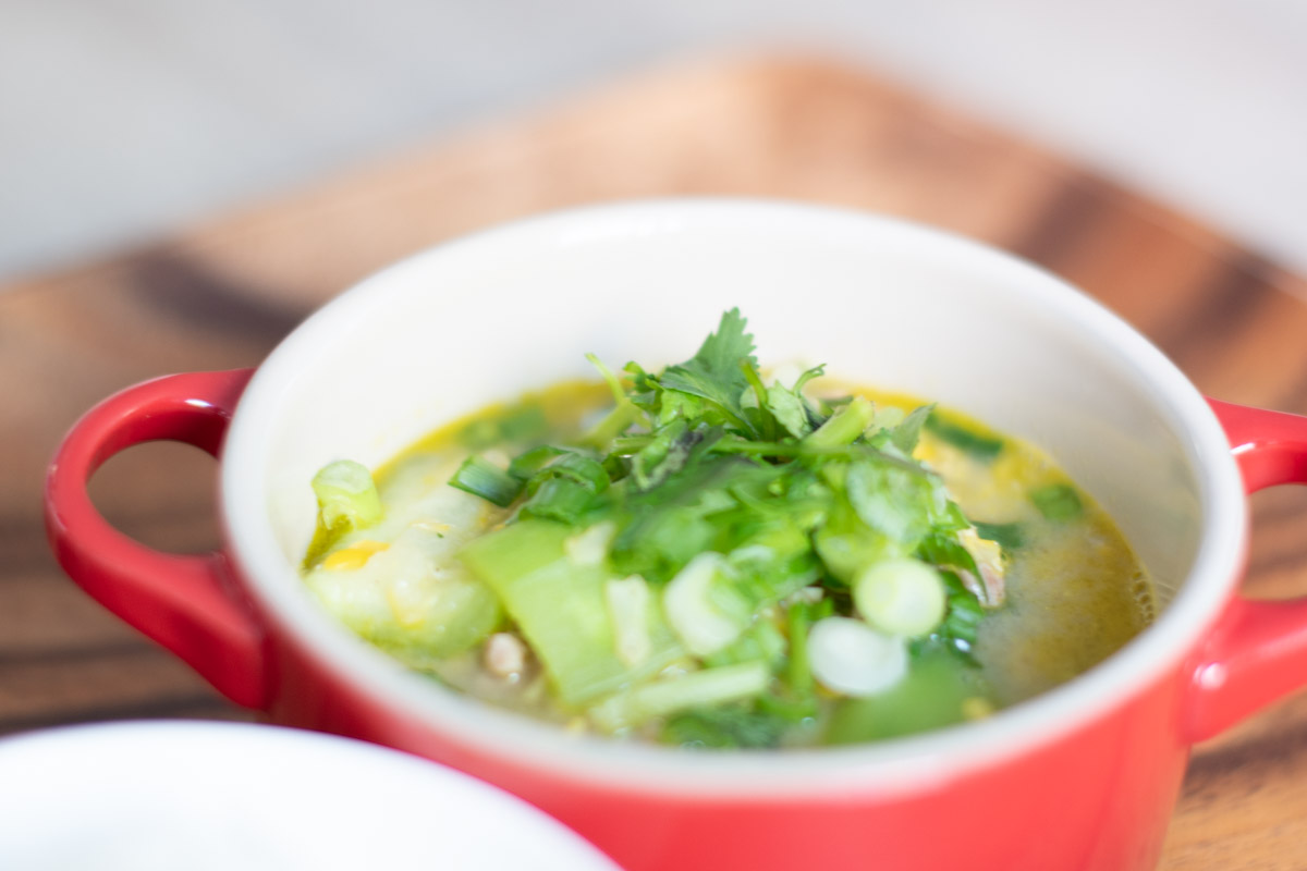 Cambodian Okra and Corn Stew served in small red stoneware pot garnished with cilantro.