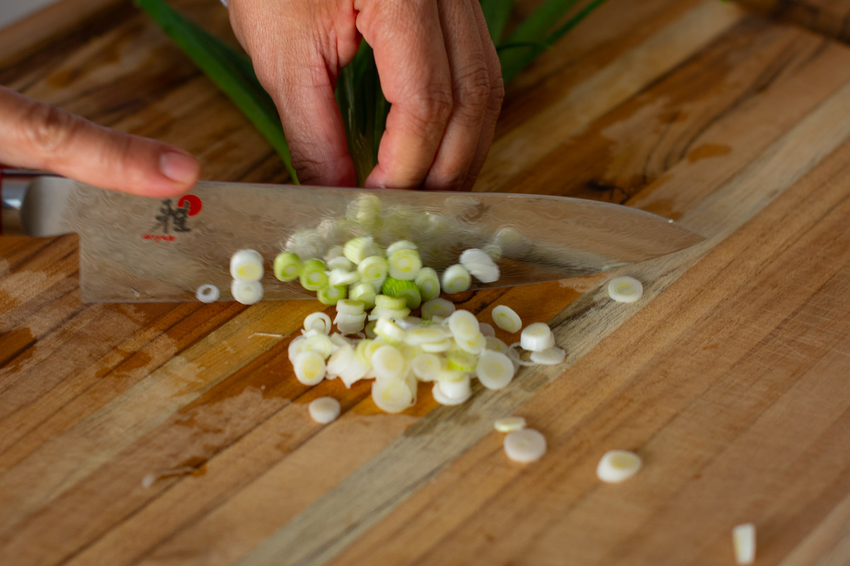 Close-up of fresh green onions being sliced for Vegetarian Cambodian Chow Mein.