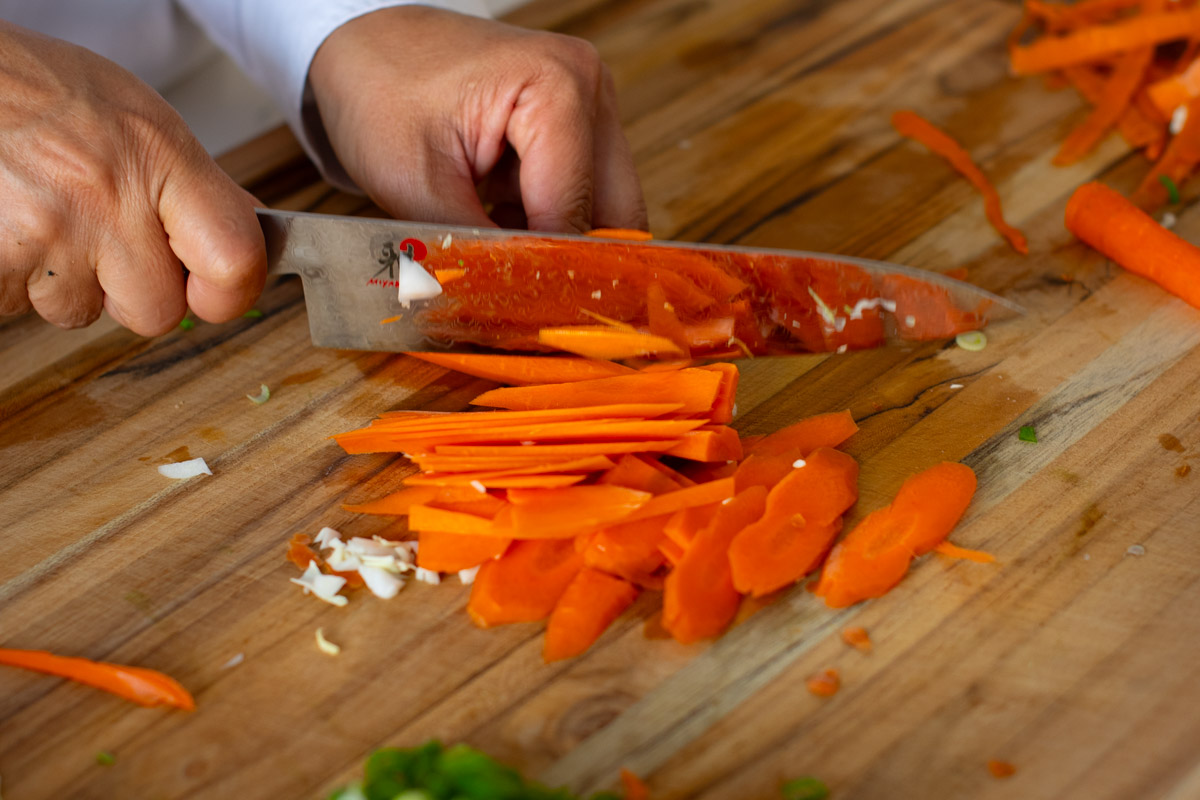 Slicing carrots into thin matchsticks for Cambodian vegetarian stir-fry noodles.