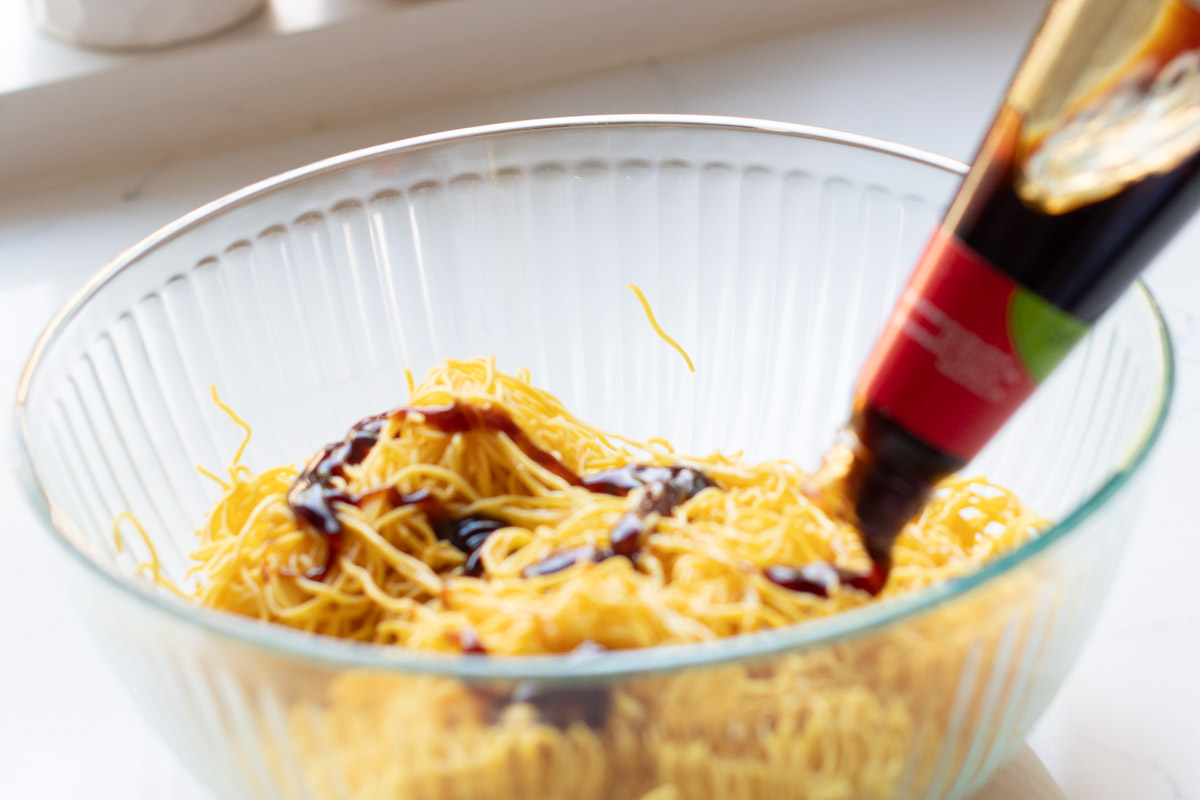 Pouring vegan oyster sauce over noodles to create flavorful stir-fry sauce.