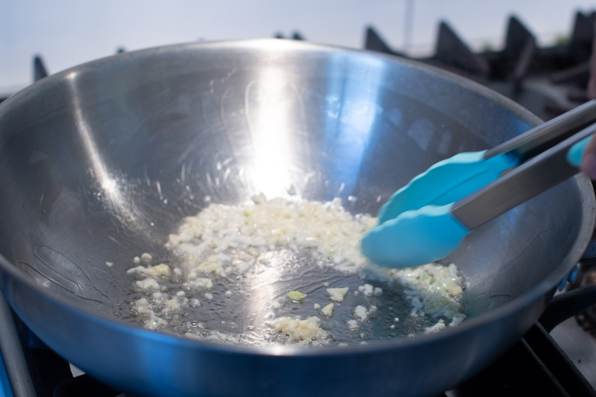 Garlic sizzling in hot olive oil for Cambodian vegetarian noodle stir-fry.