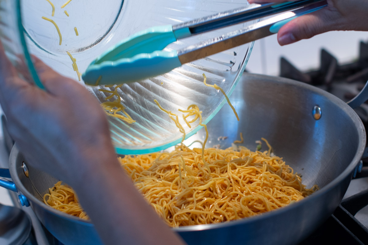 Chow mein noodles being stir-fried in a wok for Mee Cha Jay.